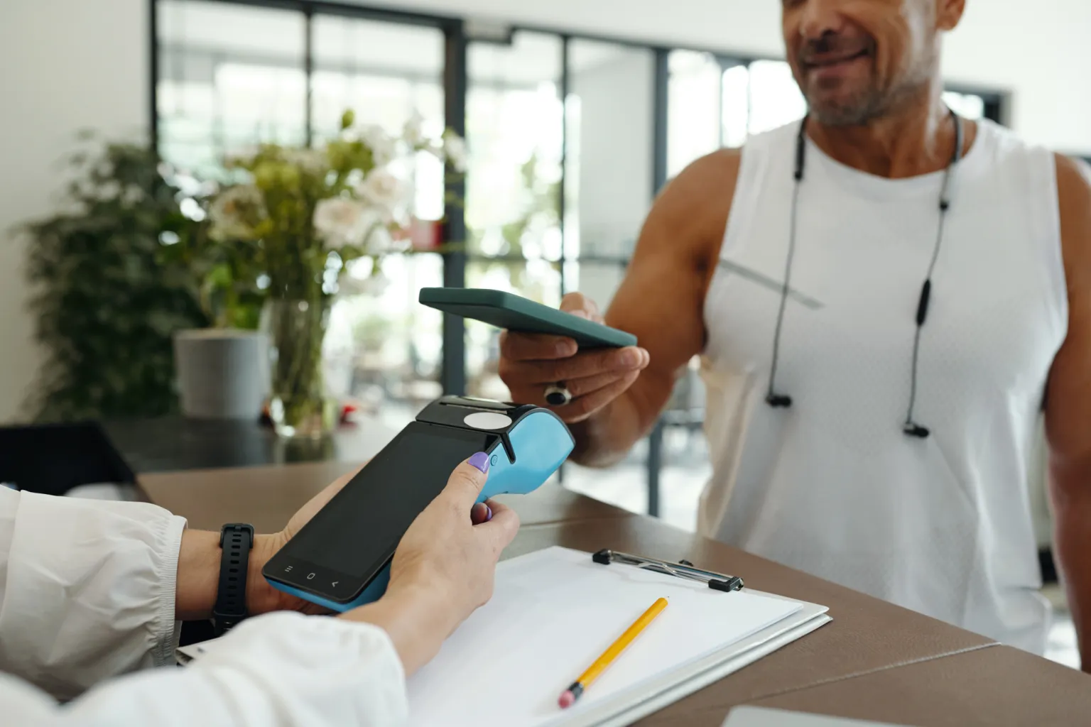 A member taps their phone to pay on an in-person terminal at the front desk
